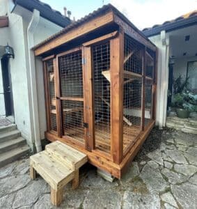 Large wooden screened in outdoor space on the side of a house for cats termed a catio